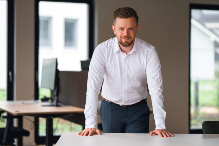 Benedikt Gondolf steht im Büro und stützt sich auf einen Tisch