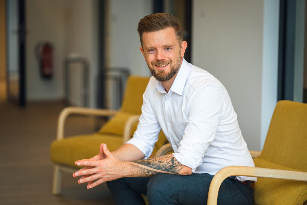 Benedikt Gondolf sitzt auf einem gelben Sessel im Büro