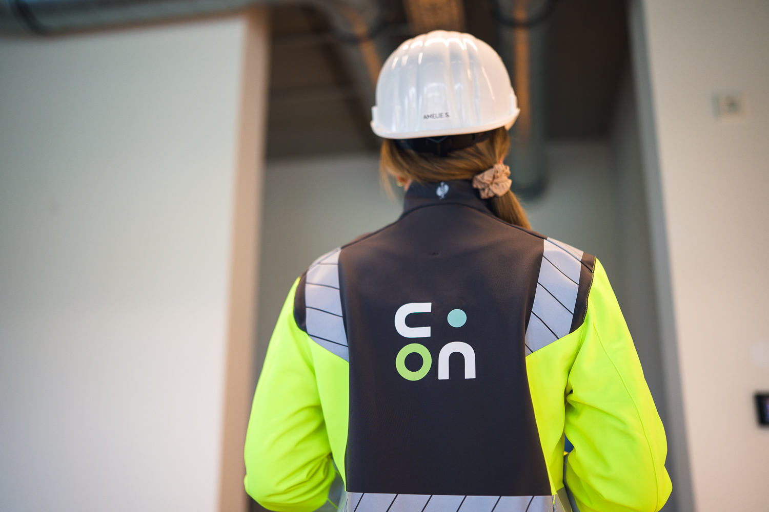 Projektleiterin mit Schutzhelm und clary.ON-Weste in einer Industriehalle